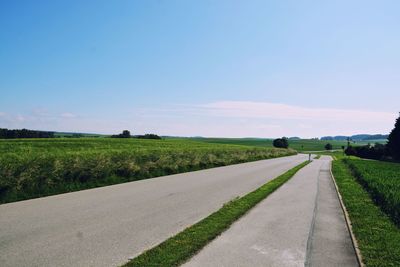 Empty road amidst field against sky