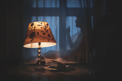 Close-up of electric lamp on table with shadow of woman on window