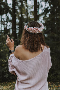 Rear view of woman wearing flowers standing at forest
