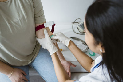 High angle view of doctor piercing needle in patient's arm for medical exam in clinic