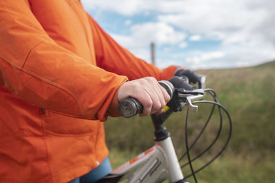 Detail of the hands of a young woman wearing an orange jacket on the handlebars of her bicycle