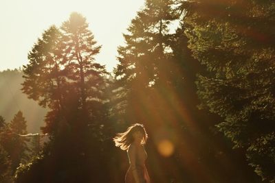 Side view of woman standing against trees in forest