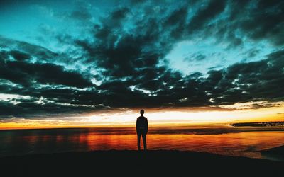 Silhouette man standing on beach against dramatic sky