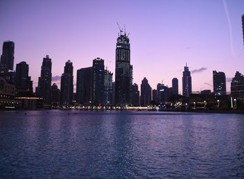 Sea by illuminated buildings against sky at dusk