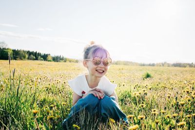 Young girl sat with sunglasses on in a field of flowers in summer