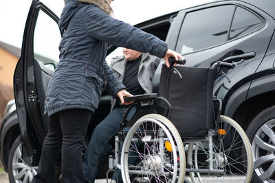 A woman helps aphysical disabled person to get into the car.