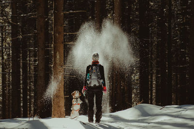 Rear view of young woman playing by dog with snow