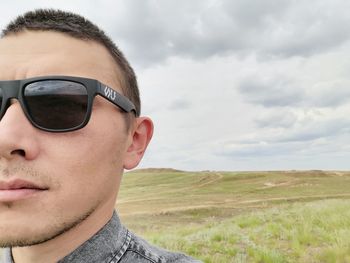 Portrait of young man wearing sunglasses on field against sky