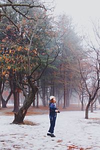 Full length of woman standing by trees on field during winter