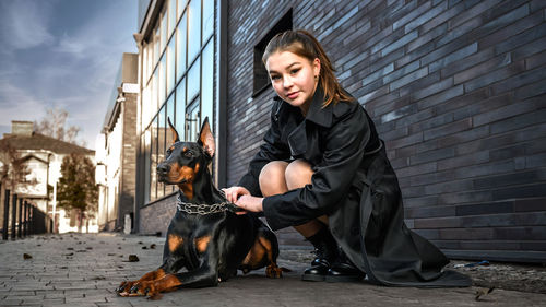 Teenage girl sitting next to a dog on the street. girl hugging her dog in urban environment. 