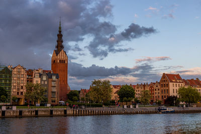 Buildings at waterfront against cloudy sky