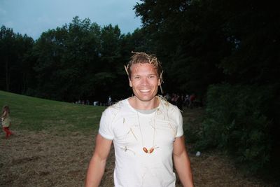 Portrait of happy man standing at field with straw on hair