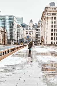 Rear view of man walking on wet street in city