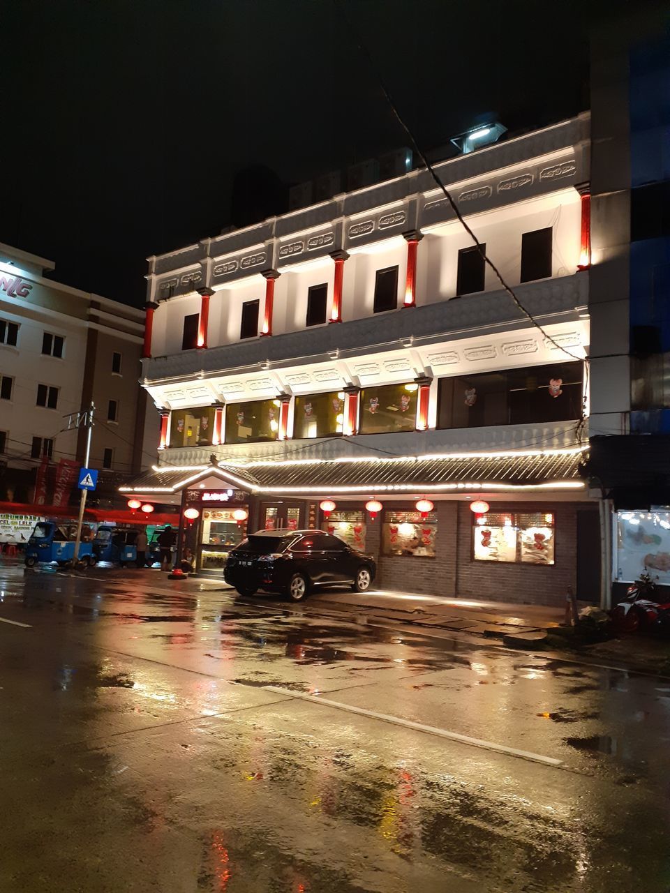 WET ROAD BY ILLUMINATED BUILDINGS DURING RAINY SEASON