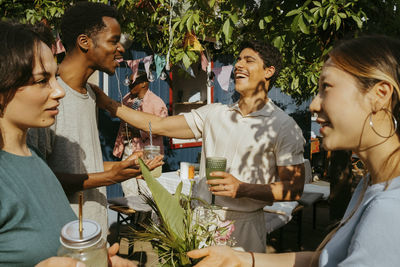 Happy multiracial male and female friends talking with each other while enjoying drinks at party