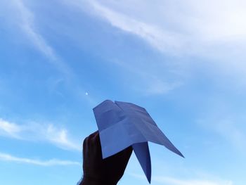 Low angle view of hand holding paper airplane against sky