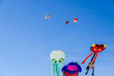 Low angle view of people paragliding against clear blue sky