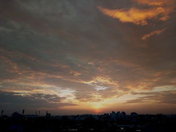 Silhouette of city against cloudy sky during sunset