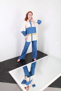 Full length of woman standing by mirror against white wall