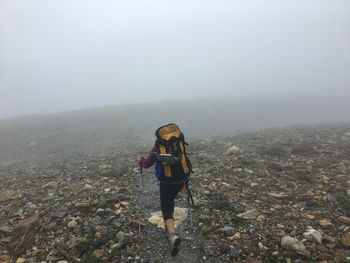 Rear view of woman standing on mountain against sky during foggy weather