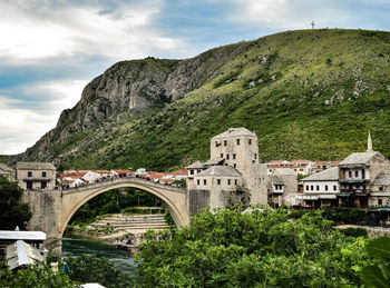 Arch bridge amidst buildings and mountains against sky