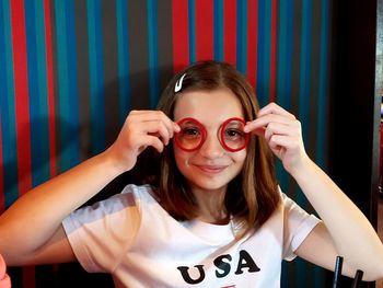 Portrait of girl holding rubber bands over eyes against wall