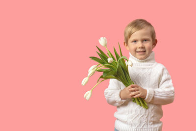 Portrait of smiling boy holding flower against red background