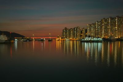 Illuminated buildings by river against sky at night