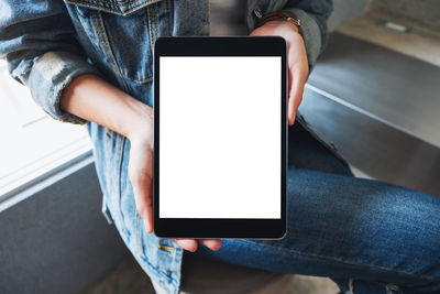 Midsection of woman using digital tablet by window