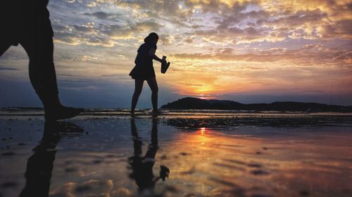 Silhouette people standing on beach against sky during sunset