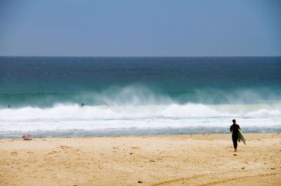 Rear view of man with surfboard walking at beach