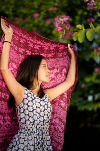 Low angle view of young woman holding pink scarf at park