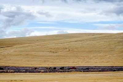 View of harvested rolling landscape against cloudy sky