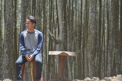 Young man sitting against trees at forest