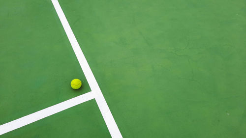 High angle view of yellow tennis ball on green tennis court 