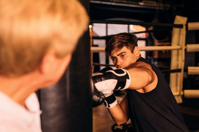 Instructor standing by boxer punching bag in boxing ring