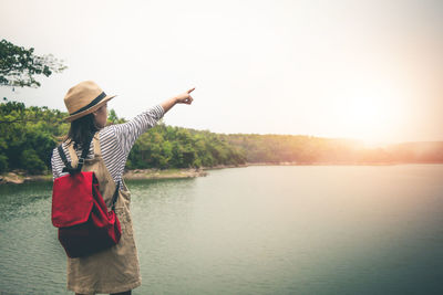 Rear view of woman standing by lake against sky