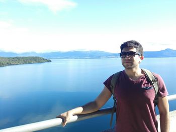 Portrait of young man standing by railing against lake