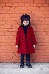 Korean girl in a red coat and cap and round glasses stands on red brick wall the street in autumn