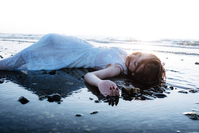 Woman lying at beach against sky