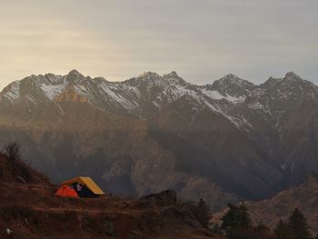 Scenic view of snowcapped mountains against sky, at sunset with people ina tent camping.