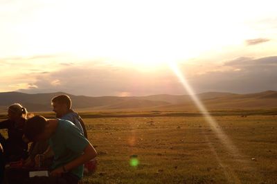 Rear view of people on field against sky during sunset