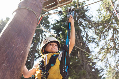 Low angle portrait of boy holding rope against trees