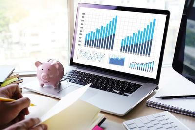 Cropped image of business person working at desk by laptop and piggy bank in office