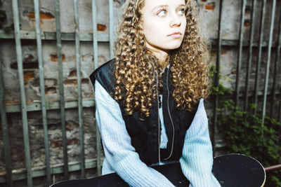 Contemplative girl with curly hair looking away against wall