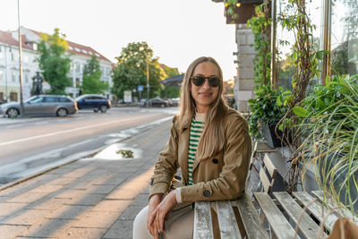 Portrait of young woman sitting on footpath in city