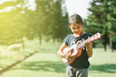 Girl playing guitar while standing on grassy field at park