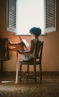 Side view of woman sitting on chair at home holding a book and a machete 