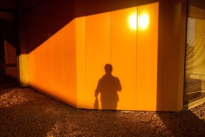 Silhouette man standing by illuminated yellow light at sunset