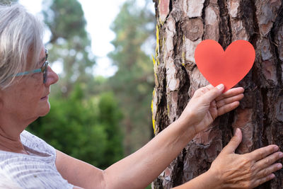 Midsection of woman holding heart shape on tree trunk